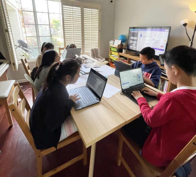 Children sitting at a table and using AIStory on their laptops.
