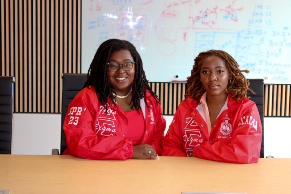 Jazette Johnson and Lucretia Williams sitting next to each other and wearing their sorority's Delta Sigma Theta jackets.