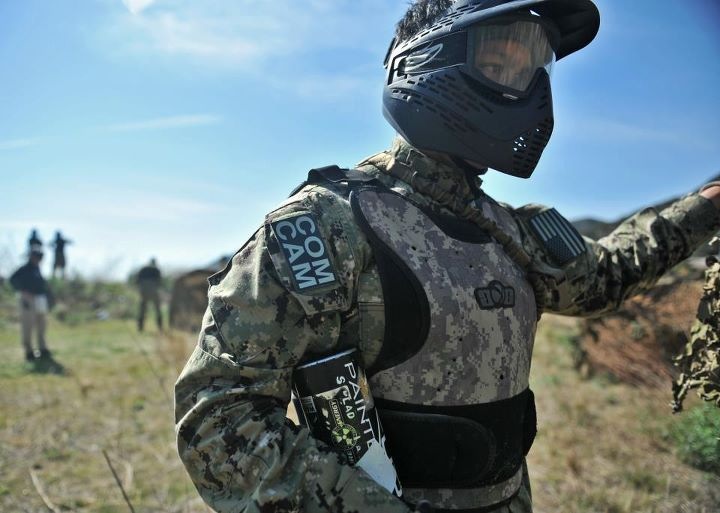 Balacy wearing a helmet and camouflage gear, in a field with others in the backdrop.