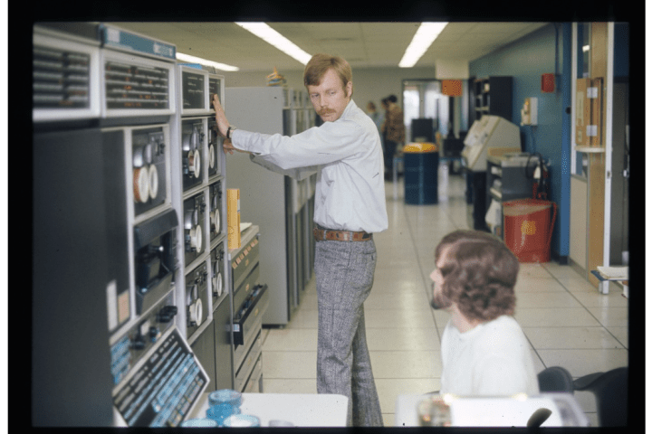 Two men near a wall-sized computing system.
