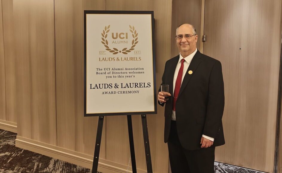 Steve Acterman stands in front of a sign that says, “The UCI Alumni Association Board of Directors welcomes you to this year’s Lauds & Laurels Award Ceremony.”