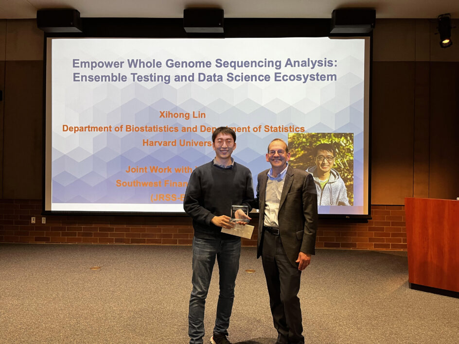 Qi Xu holding an award next to Hal Stern. Behind them, the screen shows the upcoming talk by Xihong Lin on "Empower Whole Genome Sequencing Analysis"
