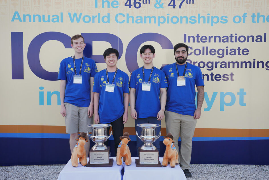 Four students standing in front of a backdrop that says ICPC in Egypt.