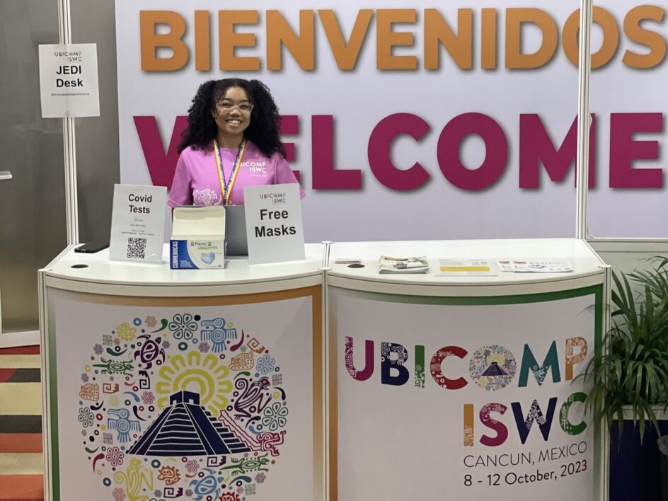 Vitica stands at a booth that says “Bienvenidos/Welcome to Ubicomp.”