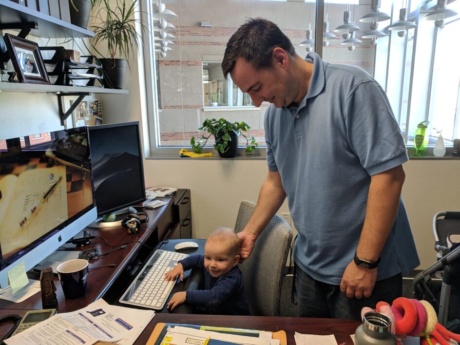 Gago-Masague stands behind a chair where his baby sits, hands on a keyboard.