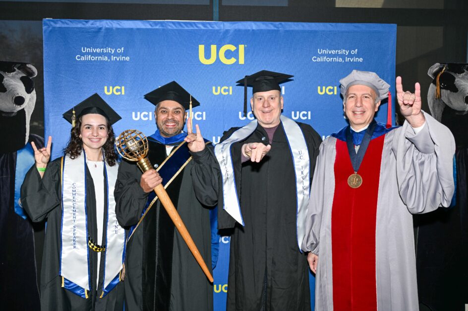 The group of four, in front of a UCI backdrop, showing the “anteater face” with their hands, where the two middle fingers touch the thumb while the index and pinky fingers remain up.