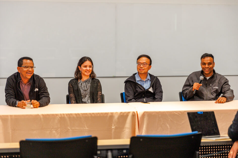 Four people sit at table, with one person holding a microphone.