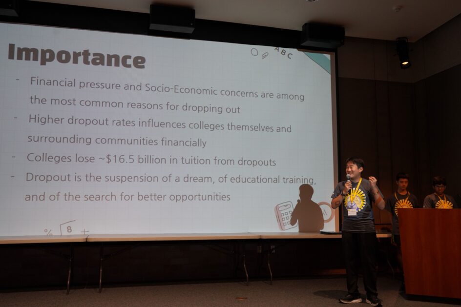 A student with a microphone stands in front of a large screen