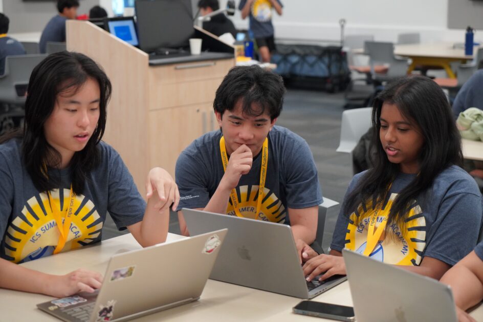 Three students work together at a table with laptops