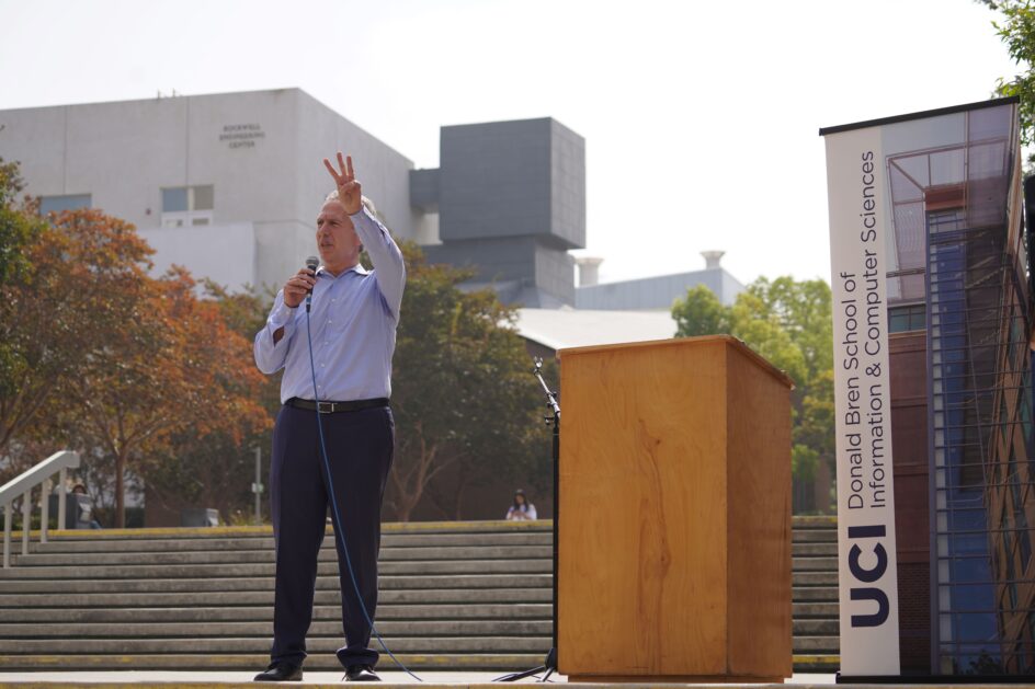 Dean Marios stands near a podium holding up three fingers.