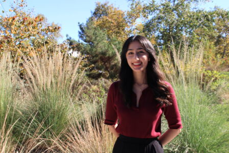 Minal Walvekar smiling and standing in front of tall grasses and trees.