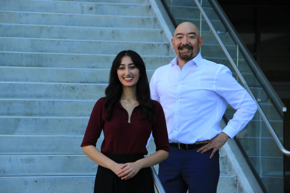 Minal Walvekar and Jonathan Watanabe smile, standing in front of concrete steps.