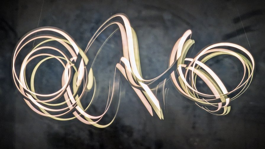 A circular-helix hanging lamp, reflected multiple times in the glass sheets of a sliding patio door